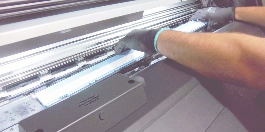 Técnico com luvas realizando manutenção no carro de impressão de plotter de grande formato